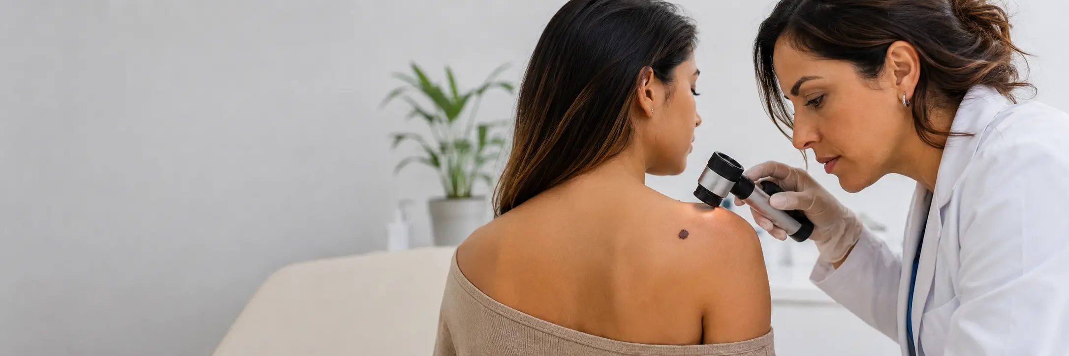 Dermatóloga revisando con dermatoscopio un lunar pigmentado en la espalda de una paciente como parte de la evaluación del ABCDE del melanoma.